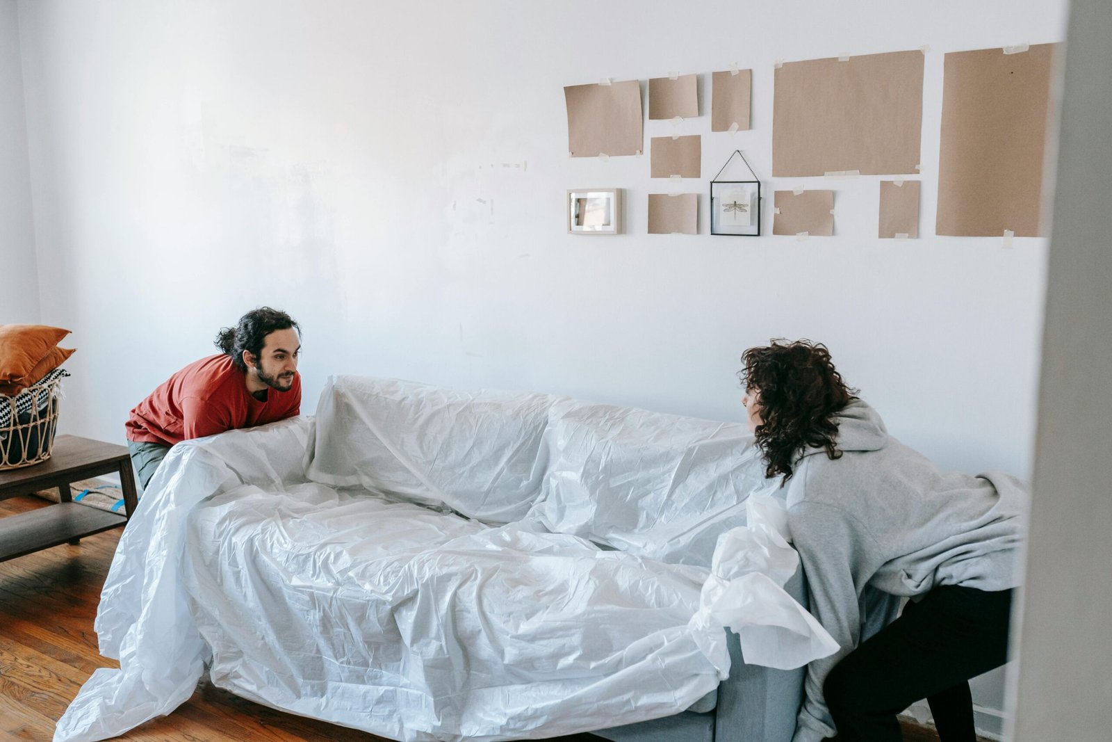 A couple rearranging furniture in their new apartment, lifting a wrapped couch together.